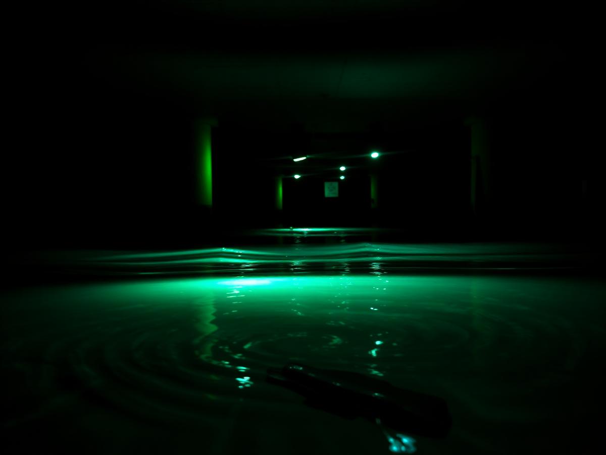 Close-up of underwater dock lights glowing electric green through ripples